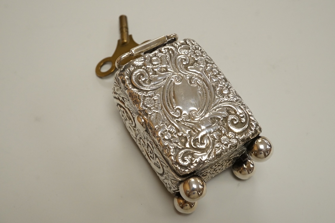 An early 20th century white metal (tests as silver) carriage timepiece, with white Roman dial (cracks) and case embossed with foliage, on four ball feet, 76mm excluding handle, with key.